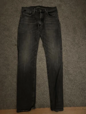 Mörk gråa slim jeans från Polo Ralph Lauren - Snygga mörk gråa jeans från Polo Ralph Lauren med slim passform och klassisk femficksdesign. Jeansen har diskreta slitningar och grå toning längs benen för en cool look. Materialet är jeans med tydliga sömmar och knappstängning framtill.