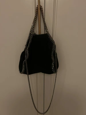 Svart Stella McCartney Falabela M - Hej, säljer nu min as Snygg svarta   Stella McCartney väska. Väskan har silverfärgade kedjor som axelrem och vanliga handag samt runt kanterna. Väskan har magnetlås och ett ljusrosa innerfoder med logotyp. Jag säljer min älskade väska nu för att den tyvär inte kommer till andvändning längre🥹 Vid snabb affär så kan priset diskuteras❤️
