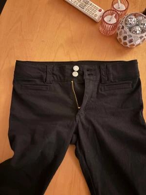 Svarta jeans med dubbelknapp - Snygga svarta jeans med två silverfärgade knappar och guldfärgad dragkedja. Klassisk femficksdesign och smal passform. Perfekta för dig som gillar stilrena och enkla byxor med en modern touch.