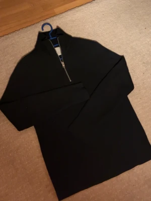 Svart stickad half zip från Jack & Jones - Svart stickad tröja från Jack & Jones med half zip och hög krage. Tröjan har långärmade ribbade ärmar och är gjord i ett mjukt material som passar perfekt när det är lite kyligt ute. Enkel och stilren design som funkar till många olika outfits.
