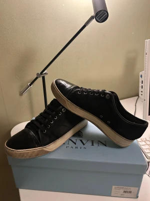 Lanvin cap toe  - Säljer ett par svarta sneakers från Lanvin med snygg kontrast mellan matt textil och glansigt skinn på tån. Skorna har vita sulor, svarta snören och metallfärgade öljetter. Perfekta för dig som gillar stilrena och exklusiva sneakers med en lyxig känsla.