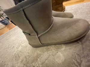 Gråa boots från din sko i mocka - Säljer ett par sprillans nya grå boots från din sko med rund tå och platt sula. Tillverkade i mjuk mocka med synliga sömmar och högt skaft som håller värmen. Perfekta för kalla dagar och har en enkel, stilren look.💘💘