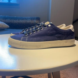 Blå mockasneakers Polo Ralph Lauren - Snygga blå sneakers från Polo Ralph Lauren i mocka med vita detaljer och silverfärgad plös. Klassisk låg modell med vita sulor och svarta snören, extra vita skosnören medföljer. Insida i skinn och textil för extra komfort. Använda 1 gång