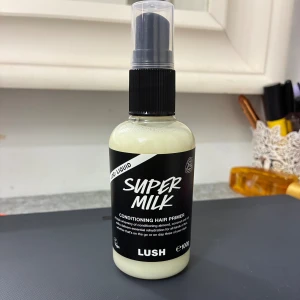 Super Milk Conditioning Hair Primer - Super Milk Conditioning Hair Primer från Lush i en smidig pumpflaska. Vit, krämig formula med mandel, kokos och havre för återfuktning och mjukhet. Perfekt för att förbereda håret innan styling. 100g.