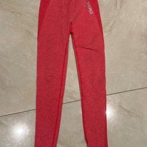 Röda träningstights från Rapid wear thights  - Snygga röda träningstights från Rapid med hög midja och tight passform. Tillverkade i ett stretchigt syntetmaterial som sitter skönt och följer kroppen. Perfekta för gymmet eller löprundan.