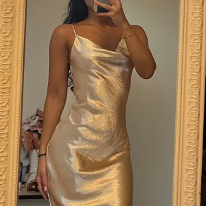 Champagnefärgad satin klänning - Säljer en  champagnefärgad långklänning i glansig satin med smala axelband och öppen rygg. Klänningen har en snygg draperad halsringning och figurnära passform 