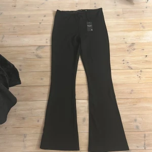 Svarta bootcut byxor Black Label - Svarta bootcut byxor från The Black Label Collection. Byxorna har hög midja och är tillverkade i ett mjukt, stretchigt material som sitter snyggt. Perfekta för dig som gillar en stilren och trendig look med utsvängda ben.