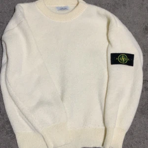 Vit stickad tröja från Stone Island - Säljer en clean vit stickad tröja från Stone Island med klassisk patch på ärmen. Tröjan har rund halsringning, ribbade muddar och är långärmad. Perfekt för dig som gillar stilrena och exklusiva plagg. Priset kan diskuteras🔥👌