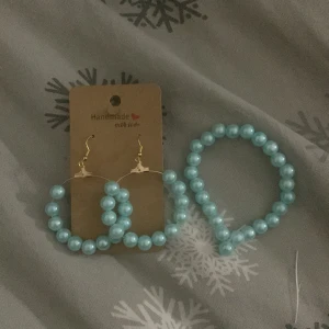 Turkost pärlset örhängen & armband - Säljer ett handgjort smyckeset med stora turkosa pärlor. Setet består av ett par creolörhängen med guldfärgade krokar och ett matchande elastiskt armband. Perfekt för dig som vill sticka ut med färg och pärlor.