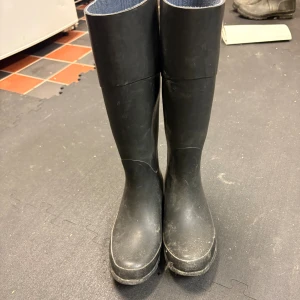 Mörkblå höga gummistövlar med snörning - Mörkblå höga gummistövlar med snörning framtill och blått textilfoder på insidan. Klassisk rund tå och platt sula, perfekta för regniga dagar. Stövlarna har en stilren look och snörningen ger en extra cool detalj. Kan tvätta av dem åt dig. Storlek 38 men något små enligt mig 
