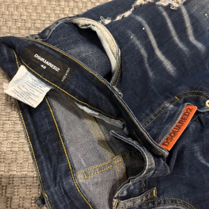 Blå jeansshorts från Dsquared2 - Säljer ett par blå jeans från Dsquared2 med slitna detaljer och coola slitningar framtill. Klassisk femficksmodell med orange Dsquared2-logga och broderad patch bak. Storlek 48