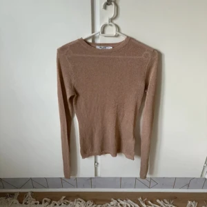 Glittrig beige tröja från NA-KD  - Supersnygg glittrig beige tröja från NA-KD i storlek XS. Tröjan har lång ärm, rund halsringning och en slim passform. Perfekt för dig som vill ha något stilrent men ändå med lite extra shine.