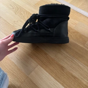 Svarta inuikki  - Säljer ett par svarta boots med grov snörning och mjuk päls på insidan. Skorna har en rund tå, platt sula och är tillverkade i mocka och skinn. Perfekta för kalla dagar och har en cool, chunky look.