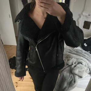 Svart teddyjacka med dragkedja - Säljer en svart teddyjacka med bred krage och mysigt foder. Jackan har en cool bikerstil med sned dragkedja, stora fickor och detaljer i metall. Perfekt för kalla dagar när du vill vara både varm och snygg.