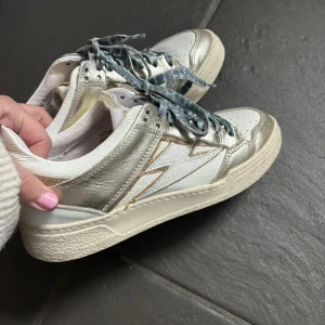 Coola sneakers - Vita sneakers med guldiga detaljer och blå leopard skosnören. Använda ca 3-4 gånger så jättefint skick!! Köpta i frankrike