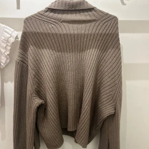 Beige ribbad polotröja - Säljer en beige ribbstickad polotröja med lång ärm och avslappnad passform. Tröjan har en hög krage och är tillverkad i ett mjukt, stickat material som känns riktigt skönt mot huden. Perfekt för lager-på-lager och chill höst- och vinterstil.