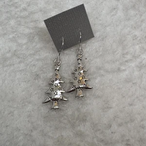 Julgransörhängen i silver - Unika örhängen i form av julgranar med små stjärnor, perfekta för att addera lite extra julkänsla till din look. Tillverkade i silverfärgat material med detaljer som glittrar lätt. Hängande modell som ger ett festligt intryck. .Tips till julkalendern