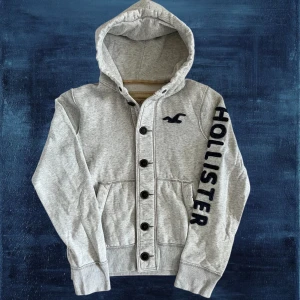 Hollister Hoodie - Säljer nu denna sjukt snygga hoodien från Hollister. OBS Storlek L men sitter mer som M, se mått. Bra skick, förutom en liten fläck på insidan av luvan, se bild 4. Inget man stör sig på då den knappt syns vid användning. Längd: 63, bredd: 54, arm: 66. Modellen är 183, 67kg. Skriv vid frågor. 