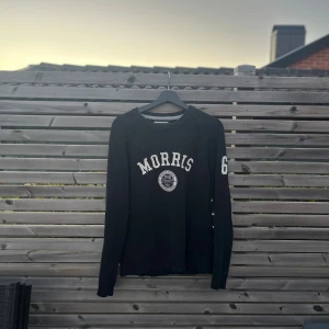 Svart stickad tröja Morris med tryck - Navy färgad stickad tröja från Morris med vitt tryck på bröstet och siffran 68 på ena ärmen. Gråa förstärkningar på armbågarna och ribbade muddar. Perfekt unikt plagg för hösten! Skriv vid eventuella frågor!