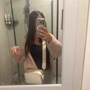 Vit axelväska från Valentino - Säljer en stilren vit axelväska från Valentino med bred justerbar axelrem och präglad logga framtill. Väskan har två dragkedjefack och är i slät skinnimitation. Perfekt storlek för mobil, plånbok och andra essentials.