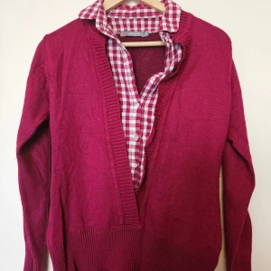 Vinröd kofta från Camaïeu Madame - Vinröd kofta från Camaïeu Madame med djup v-ringning och ribbade kanter. Koftan är långärmad och i mjukt stickat material, perfekt att slänga över en skjorta eller t-shirt. Snygg och enkel att styla till olika outfits.