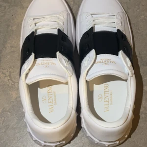 Valentino Garavani sneakers helt nya, stl 43 - Säljer ett par Valentino Garavani sneakers i storlek 43. Skorna är helt nya och aldrig använda, kommer med originalkartong. Vit modell med svart band snygg och stilren design som passar till det mesta.  Köpta i butik, äkta vara. Perfekta för dig som vill ha ett par lyxiga sneakers i toppskick till ett bra pris!