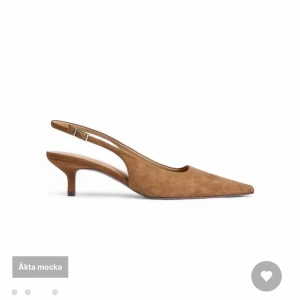 Bruna mockapumps med låg klack - Snygga pumps i äkta mocka med spetsig tå och låg klack. Skon har en öppen häl med justerbart spänne. Säljer då jag ej hann lämna tillbaka dem, aldrig använda. Nypris 799. 