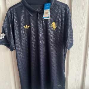 Juventus Yildiz 10 Adidas fotbollströja - Juventus fotbollströja från Adidas med Yildiz och nummer 10 på ryggen. Tröjan är mörkblå med diskret geometriskt mönster, gula detaljer och klubbmärke. Kortärmad modell i lätt funktionsmaterial med Aeroready-teknologi och Champions League-märke på ärmen.