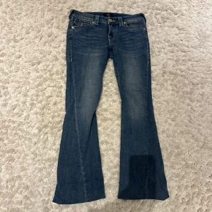 True Religion Joey Low Rise Flare Jeans - Säljer ett par blå True Religion Joey jeans med låg midja och utsvängda ben. Enbart använda ca 2-3 gånger, har inte haft de så länge, köptes i augusti.  Dessa jeans är verkligen sååå fina men tyvärr alldeles för långa för mig och det håller inte i längden att bara ha de uppnålade som jag har haft. ( jag är ca 163 ) priset är inte diskuterbart eftersom de är så nya och nästan oanvända samt inga defekter💞
