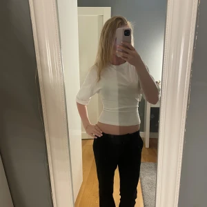 Vit T-shirt med knyt i ryggen - Säljer en vit  topp med knyt i ryggen. Toppen har korta ärmar och går att anpassa hur tajt man vill ha den i midjan. Perfekt för dig som gillar stilrena och trendiga plagg med en twist.
