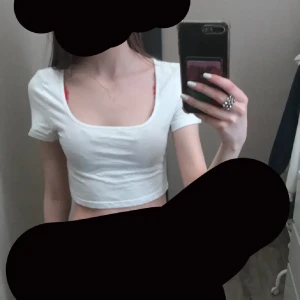 Vit croppad topp med kort ärm - Säljer en vit croppad topp med korta ärmar och rundad, djup urringning. Enkel och stilren design som passar perfekt till jeans eller kjol. Mjuk och skön bomullskänsla, perfekt för varma dagar. Snygg och fräsch look för dig som gillar minimalistiskt.