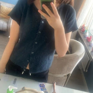 Mörkblå stickad kofta med knappar - Säljer en mörkblå stickad kofta med korta ärmar och rund hals. Koftan har en rak passform och stängs med flera knappar framtill.