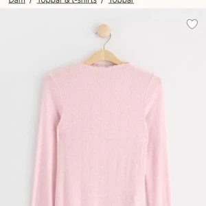 Ljusrosa ribbad topp Holly & Whyte - Supersöt ljusrosa långärmad topp från Holly & Whyte by Lindex. Toppen är ribbad med diskret struktur och har fina vågiga kanter vid hals och nederkant. Materialet är mjukt och tunt, perfekt för en chill och feminin look. Aldrig använt! Ny pris: 200kr.