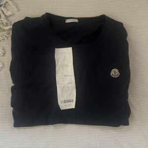 Mörkblå Moncler t-shirt i bomull - Säljer en ÄKTA monclear t shirt, tröjan är I storlek m och är blå. Ny pris på dessa är cirka 3000 kr men mitt pris är 599. Bevis finns, dock att industri tagen är borta men jag hade en bild innan med den på. Skriv vid frågor!!! Obs det är ett litet hål i tröjan.