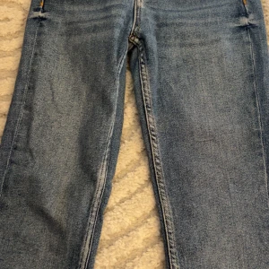 Blå raka jeans med klassisk look - Säljer ett par blå jeans med raka ben och klassisk femficksdesign. Jeansen har normal midja, tydliga kontrastsömmar och är tillverkade i robust denim. Perfekta för dig som gillar en tidlös och avslappnad stil.