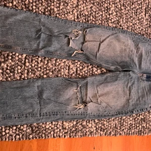  ljusblå slitna jeans från Gina - jeans med raka ben och klassisk femficksdesign från Gina. Jeansen har slitna detaljer och hål vid knäna för en cool, avslappnad look. Tillverkade i robust denim med vintagekänsla och hög midja.
