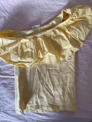 Gul offshoulder topp från Kappahl - Söt gul offshoulder topp från Kappahl med volang runt axlarna. Perfekt för varma dagar och ger en fräsch sommarkänsla. Tillverkad i mjuk bomull som är skön mot huden.