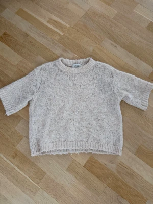 Beige stickad tröja från AWARE - Supermysig stickad tröja från AWARE i en ljusbeige ton. Tröjan har korta ärmar, rund halsringning och en relaxed fit. Perfekt för lager-på-lager och chill dagar. Materialet är mjukt och ger en skön känsla mot huden.