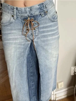 Jeanskjol med snörning från Lee - Säljer en snygg jeanskjol från Lee i klassisk blå denim. Kjolen har cool snörning framtill, femficksdesign och slits både fram och bak. Perfekt för dig som gillar en avslappnad men trendig stil. Midilängd och skön passform.
