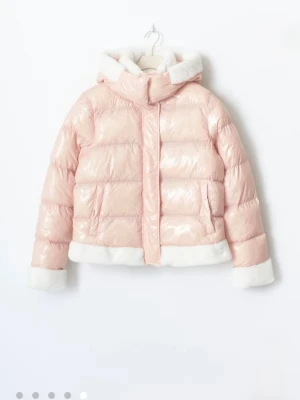 Ljusrosa pufferjacka - Superfin ljusrosa pufferjacka med glansig finish och vita fuskpälsdetaljer på huva, ärmslut och nederkant. Jackan har en hög krage, stora fickor och stängs med dragkedja och tryckknappar. Perfekt för kalla dagar när du vill sticka ut lite extra.