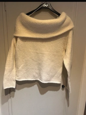 Offshoulder stickad tröja Gina Tricot - Krämvit stickad offshoulder-tröja från Gina Tricot med bred ribbad kant upptill. Tröjan har lång ärm och en loose passform som ger en avslappnad vibe. Perfekt för kyliga dagar när du vill vara både snygg och bekväm.