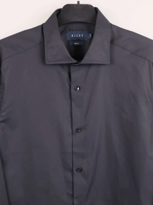 Svart slim fit skjorta från Riley - Svart skjorta från Riley i slim fit-modell, tillverkad i 100% bomull. Klassisk krage och knäppning framtill med svarta knappar. Perfekt för dig som gillar stilrena och enkla plagg med snygg passform.