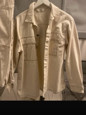 Beige kostymset från H&M, baggy - Säljer ett beige kostymset från H&M i baggy modell. Setet består av en kavaj med stora fickor och markerade sömmar samt matchande byxor med justerbar midja. Båda delar är i mjuk bomull och har en avslappnad, loose passform. Perfekt för dig som gillar en chill och trendig stil.