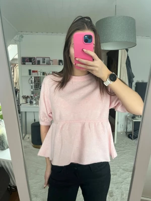 Ljusrosa stickad blus från Nelly - Säljer en ljusrosa stickad blus från Nelly med korta ärmar och volang nedtill. Den är i storlek S men passar även XS. Jag har aldrig använt den utan bara tagit bort prislappen så den är i nytt skick💕💕