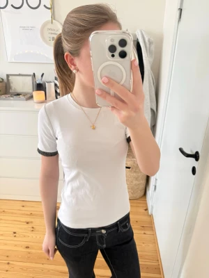 Vit t-shirt med spetsdetaljer - Vit t-shirt från Zara i bomull med korta ärmar och snygga svarta och guldiga spetsdetaljer längst ut på ärmsluten. Enkel modell med rund halsringning. Tryck gärna på köp nu!❤️