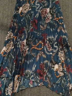 H&M vackraste  långkjol!!! - Säljer en blå långkjol från H&M Divided med blommigt mönster och coola detaljer som ormar och fjärilar. Kjolen är plisserad och har en flowy känsla, perfekt för dig som gillar statement-plagg. Midjan är normal och tyget känns lätt och luftigt.