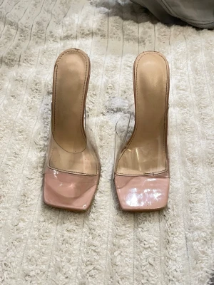Klara klackar med transparent rem - Säljer ett par trendiga klackar med fyrkantig tå och transparenta remmar. Skorna har en ljusrosa plattform och genomskinlig hög klack. Perfekta för dig som vill ha en modern och clean look. Materialet är syntet och plast.