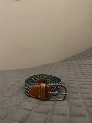 Grön vit flätat bälte - Tja det är helt nytt från Bältgallerian. Det är 105cm långt och 3,5vm brett. Det är i ett elastiskt material så passar större storlekar. Vid köpa av flera minskad priset.
