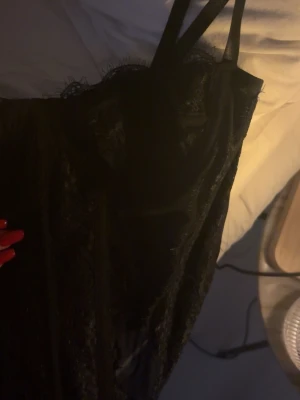 Svart spetskorsett med smala axelband - Säljer en svart korsett med smala axelband och snygga spetsdetaljer längs kanterna. Toppen har en tight passform och är tillverkad i polyester med genomskinliga partier som ger en snygg look. Perfekt för dig som vill ha något extra till outfiten.