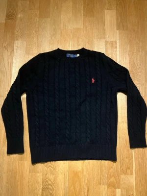 Svart kabelstickad tröja Polo Ralph Lauren - Säljer en svart kabelstickad tröja från Polo Ralph Lauren i storlek M fast den passar S. Tröjan har rund hals, långa ärmar och den klassiska röda loggan broderad på bröstet. Perfekt för kyliga dagar och riktigt snygg till jeans.